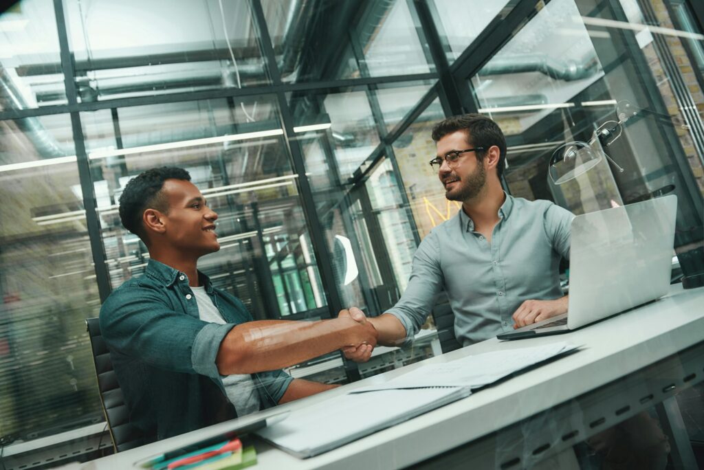 Welcome on board Two young and handsome men shaking hands and smiling while working in modern office