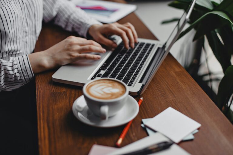 Photo of hands typing in laptop. Picture of worker behind wooden table with cup of tea and statione