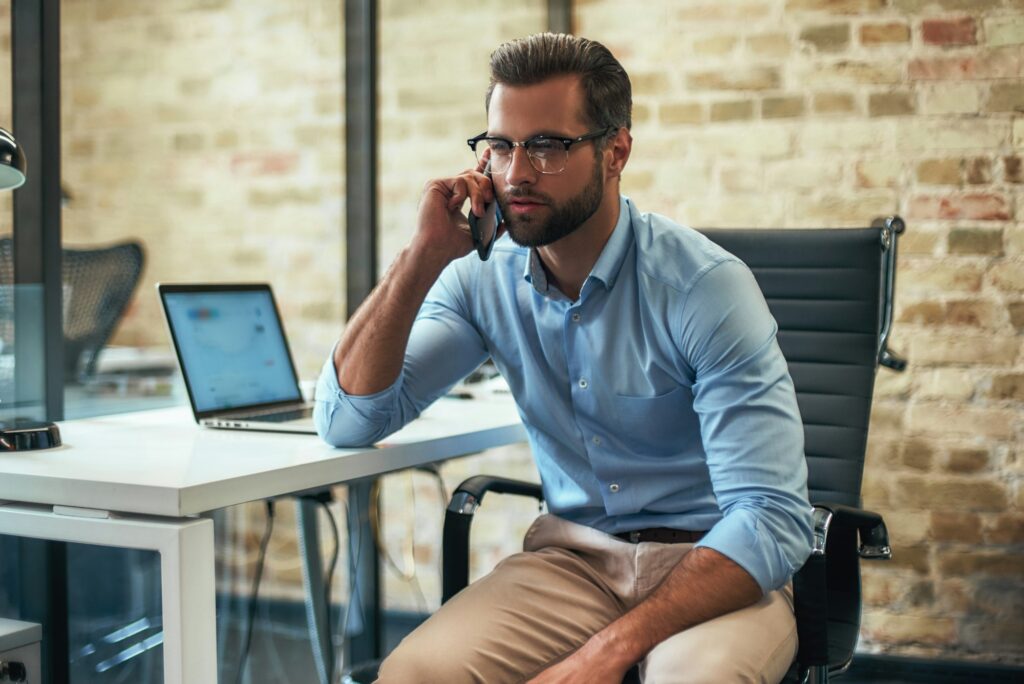 Important client. Young bearded businessman in eyeglasses and formal wear talking on the phone while