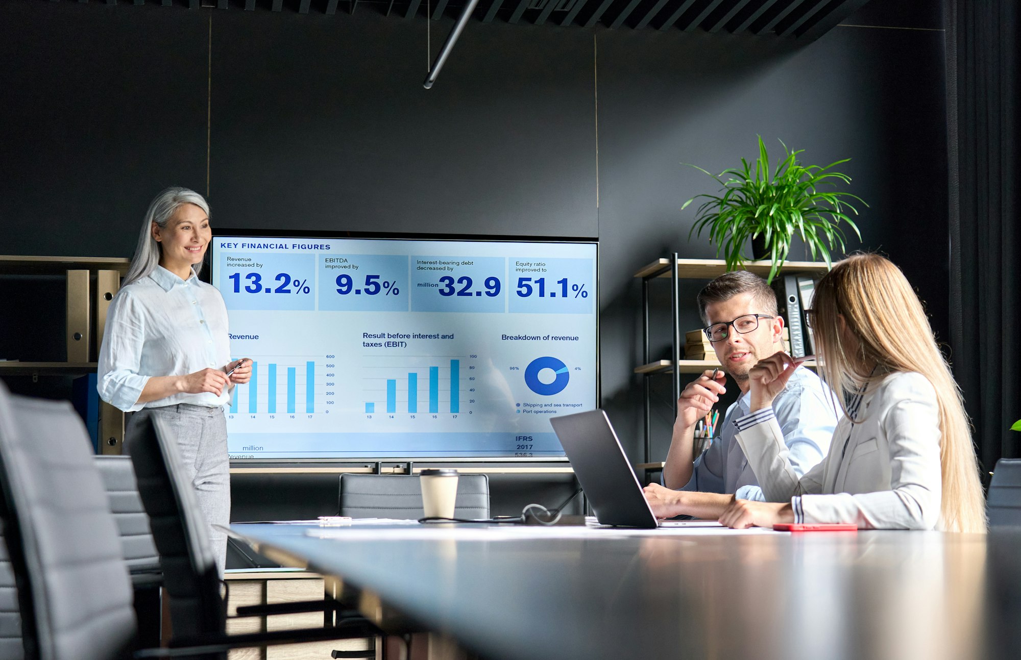 Mid age Asian female ceo presenting data to colleagues on big screen in office.