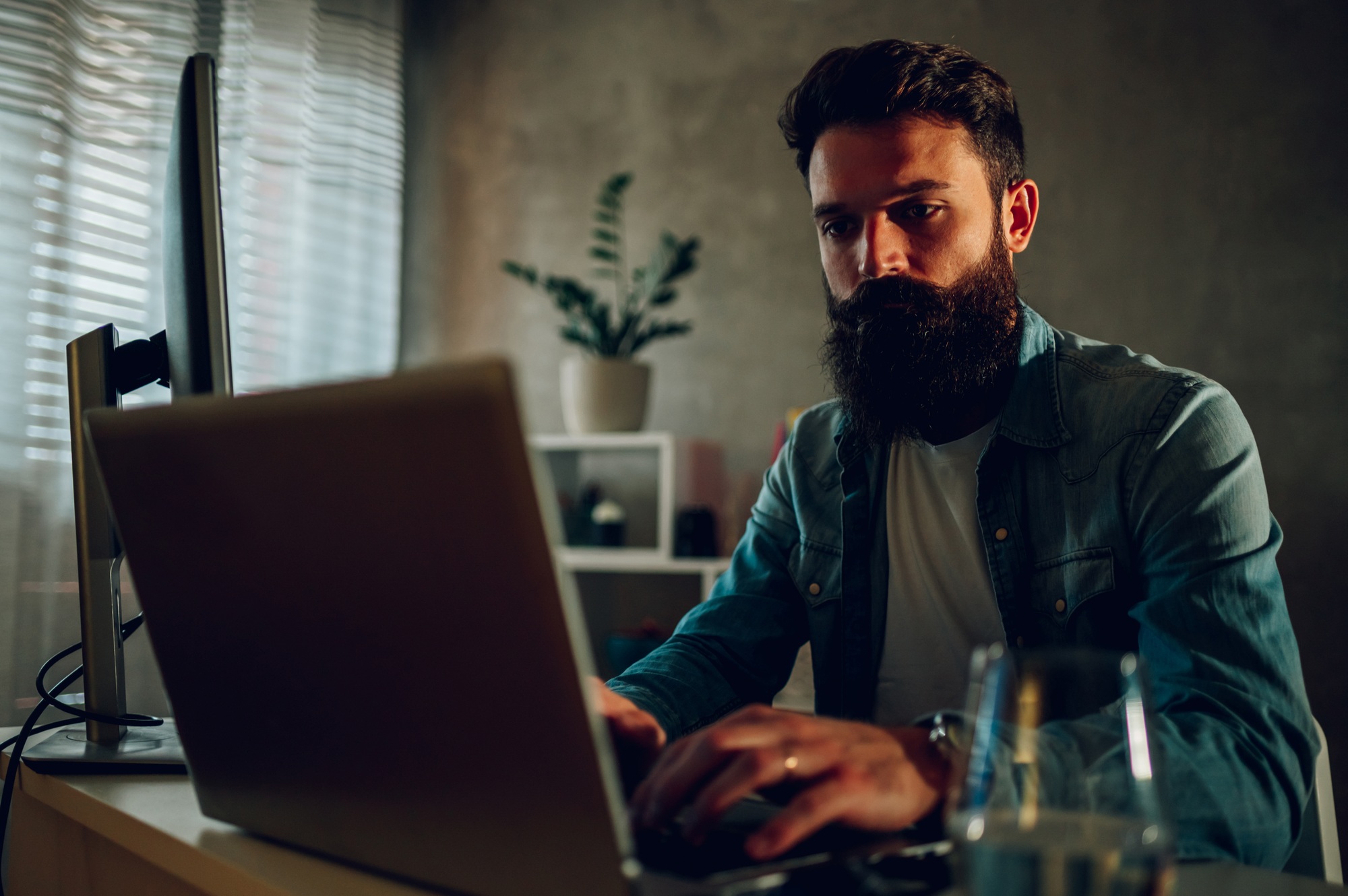 A smart software engineer is sitting in his darkened home office and developing software.