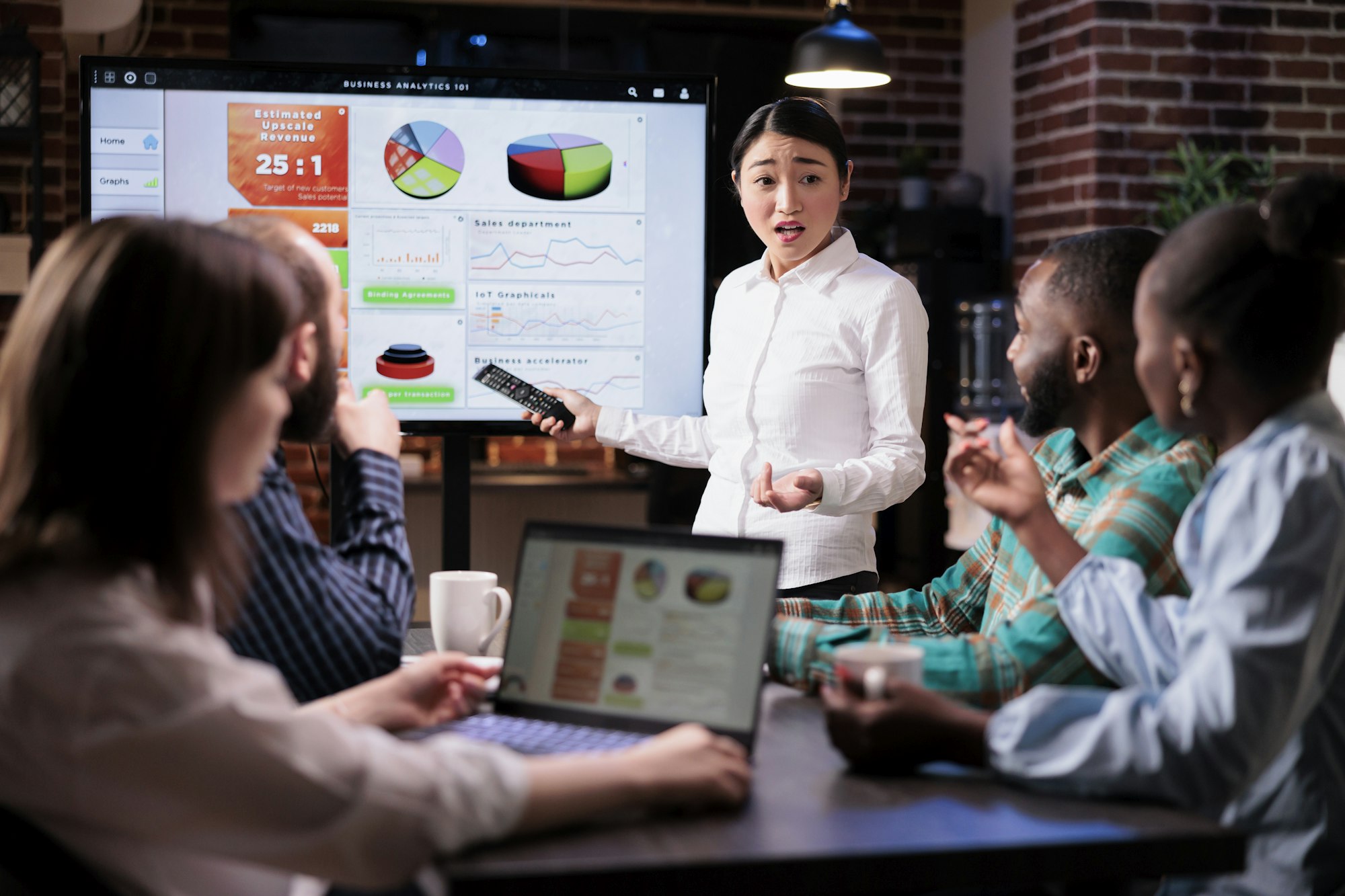 Business woman holding remote control presenting sales pie charts on tv screen working late