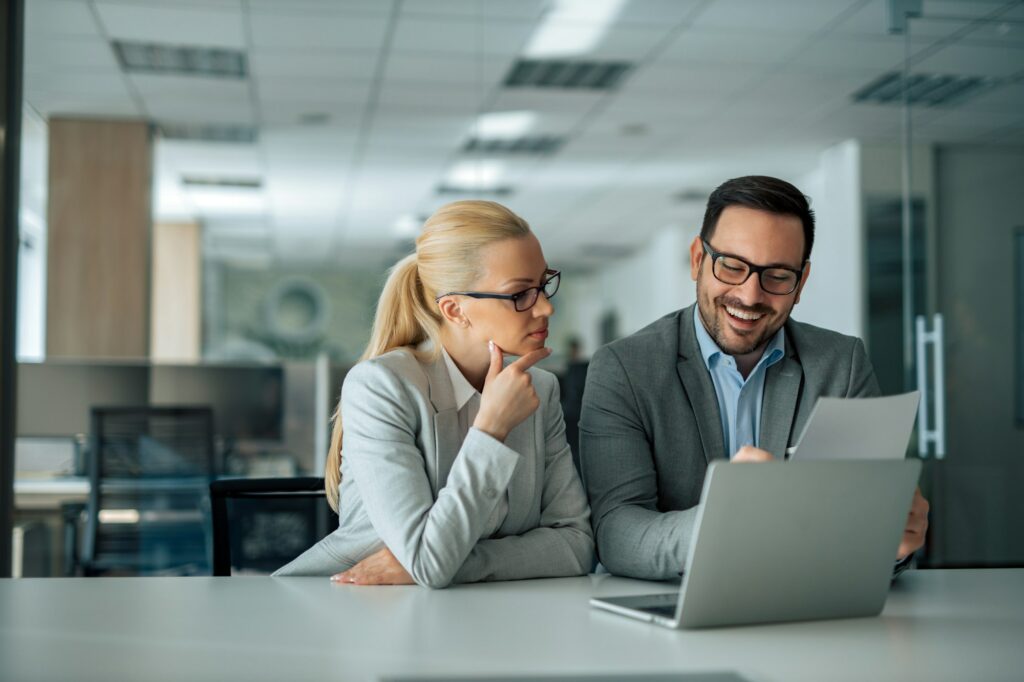 Smiling businessman showing presentation on laptop computer to a female executive, portrait.