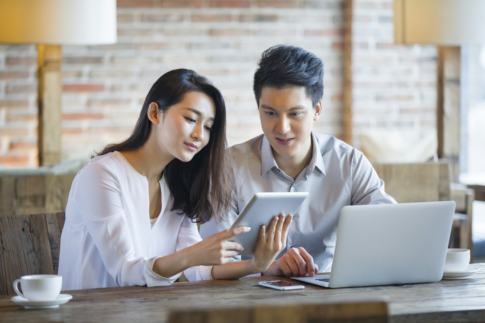 Young man and woman using digital tablet and laptop in cafe